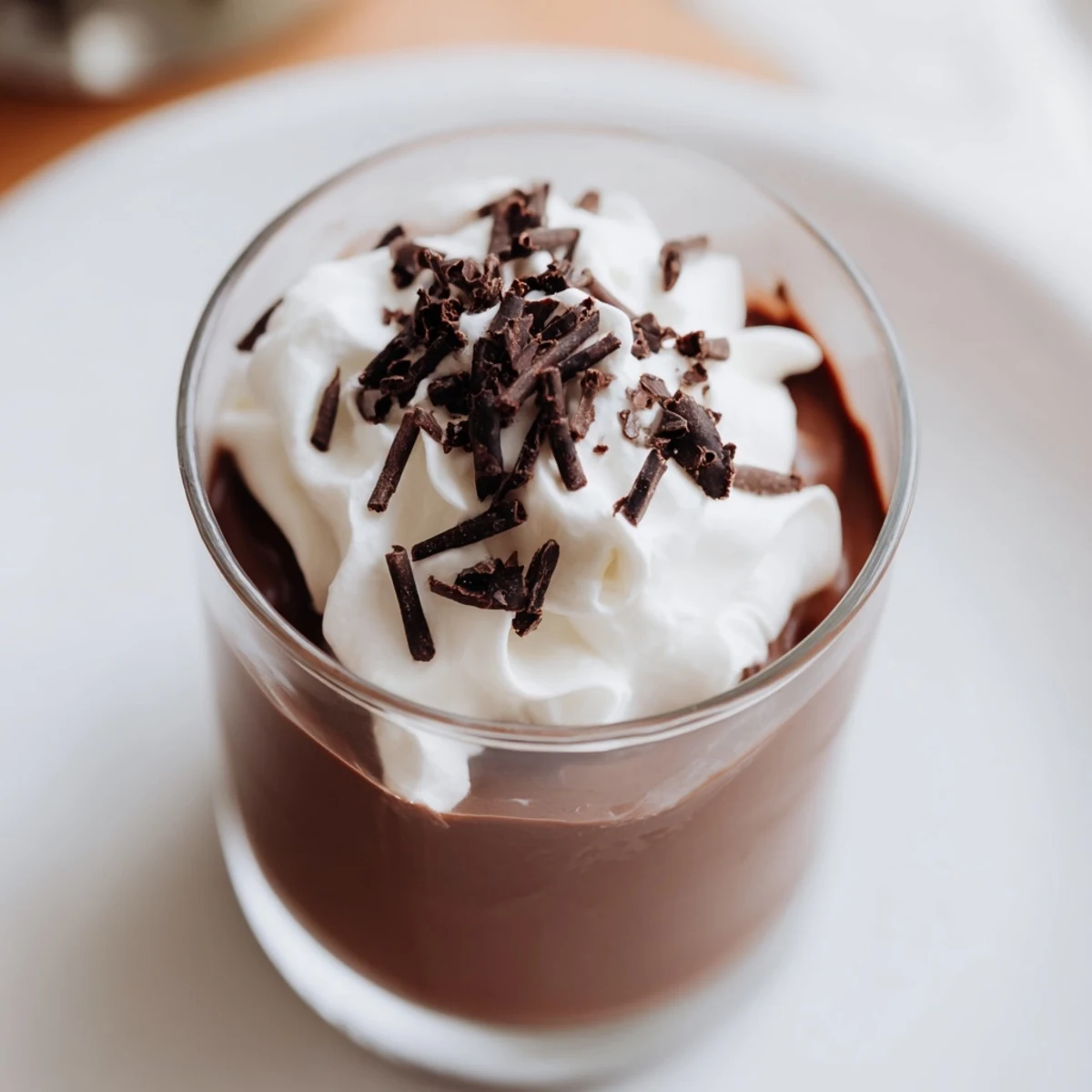 Individual chocolate pudding cups, smooth and dark, topped with whipped cream and chocolate shavings.