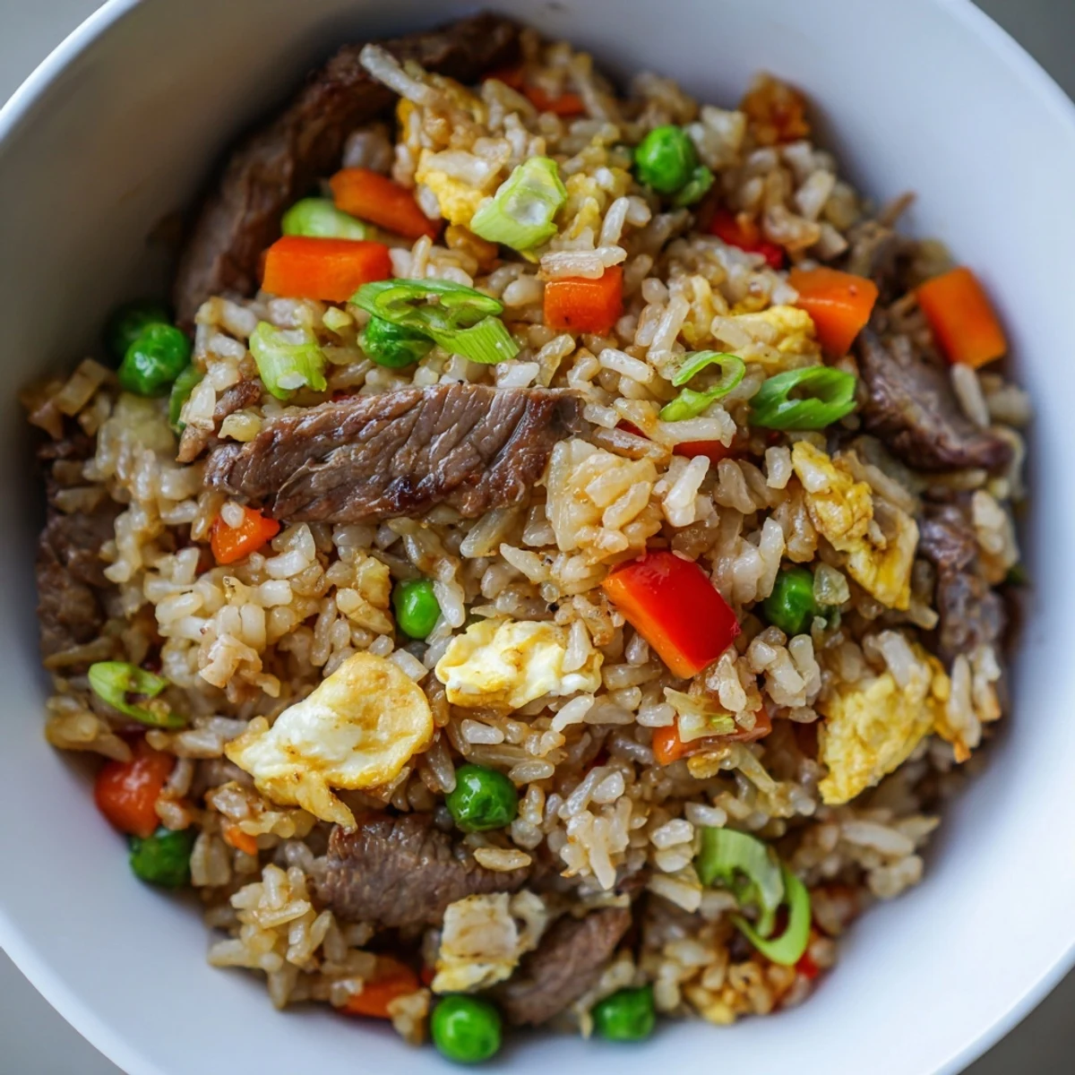 Sizzling skillet of Beef Fried Rice with Mixed Vegetables and Egg, topped with fresh green onions for a savory crunch.