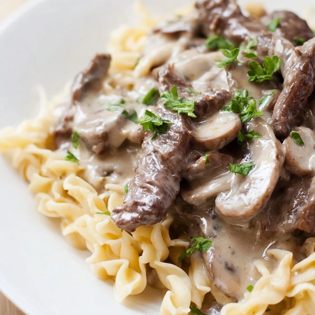 Golden-brown beef strips and sautéed mushrooms in creamy Beef and Mushroom Stroganoff, served over egg noodles with fresh parsley garnish.