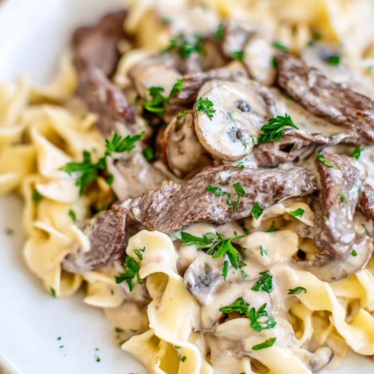 Tender beef and cremini mushrooms swimming in velvety Beef and Mushroom Stroganoff, garnished with parsley and plated for a comforting dinner.