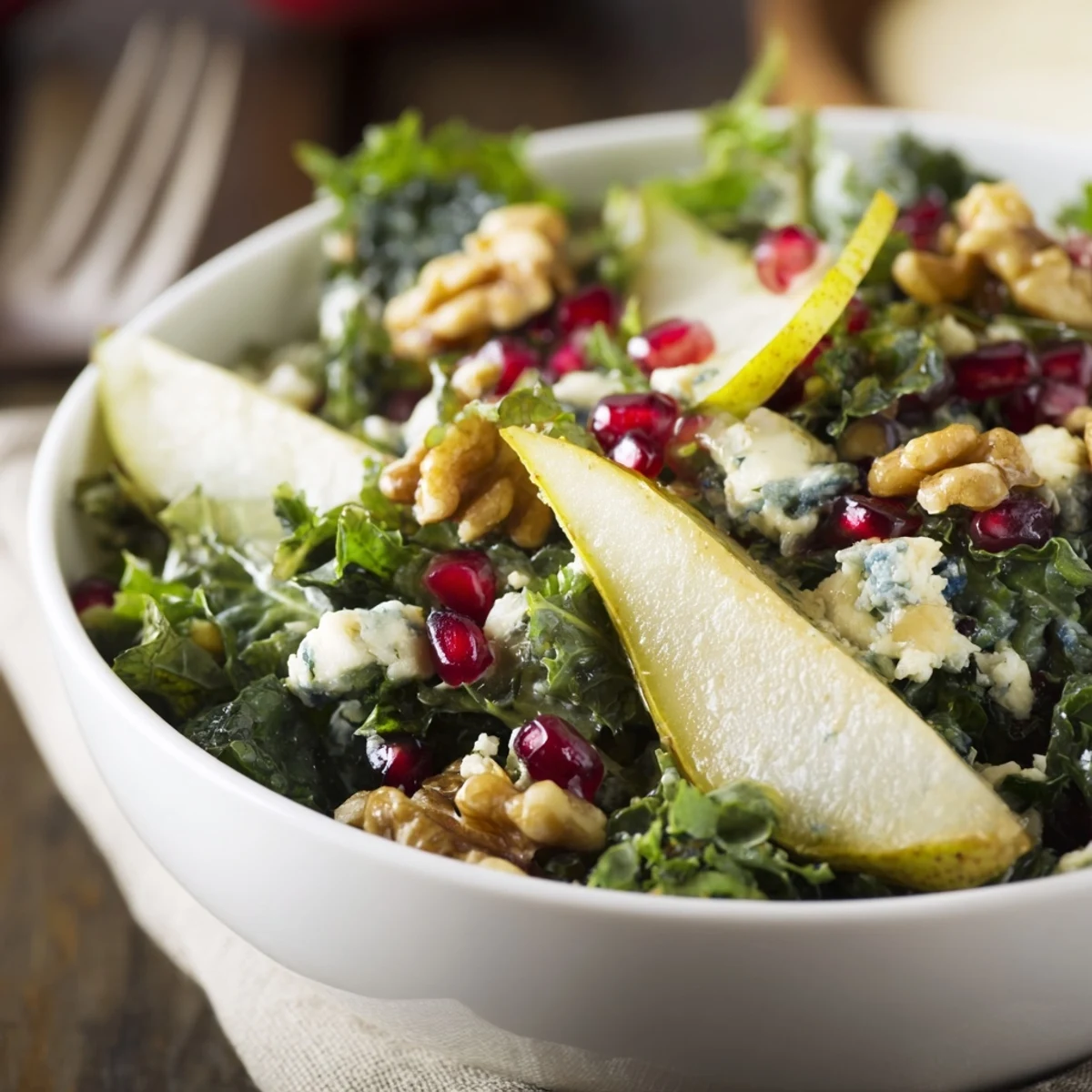 Winter Green Salad with Pear and Walnuts garnished with crumbled blue cheese and pomegranate seeds on a rustic table.