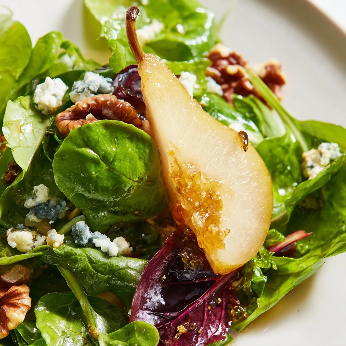 A close-up of Winter Green Salad with Pear and Candied Walnuts showing crumbled goat cheese and shiny pecan halves over vibrant kale and arugula leaves.
