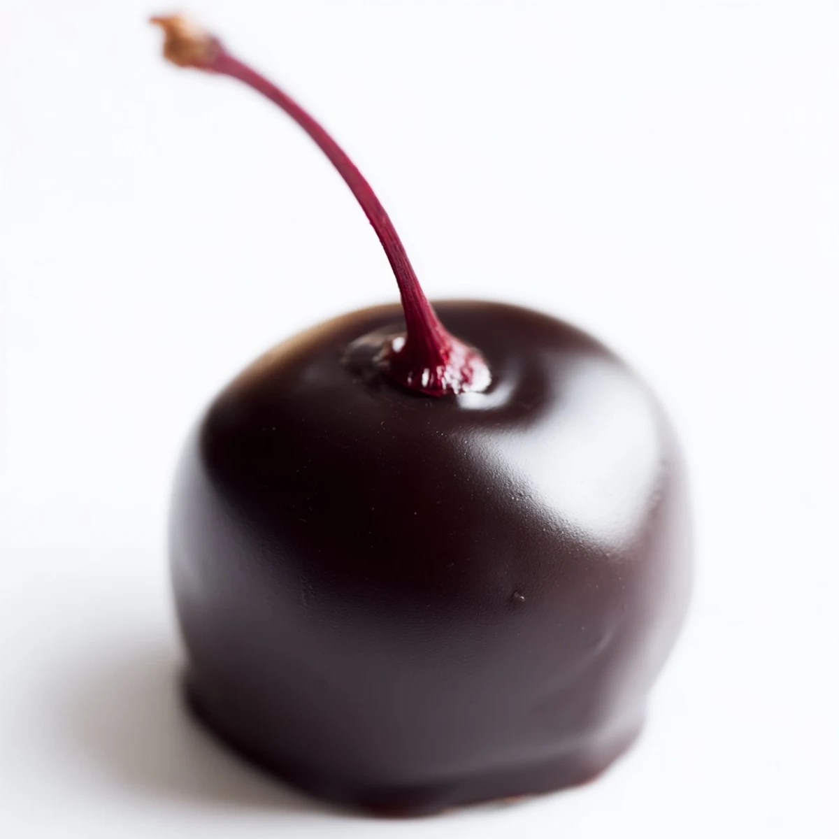 A close-up of homemade chocolate covered cherries, with dark chocolate shells glistening on parchment paper.