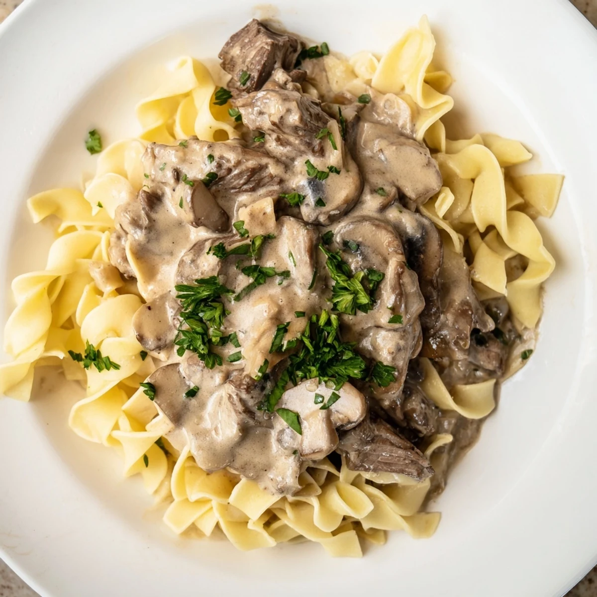 Tender beef strips and mushrooms in creamy Beef Stroganoff served over buttery egg noodles with fresh parsley garnish.