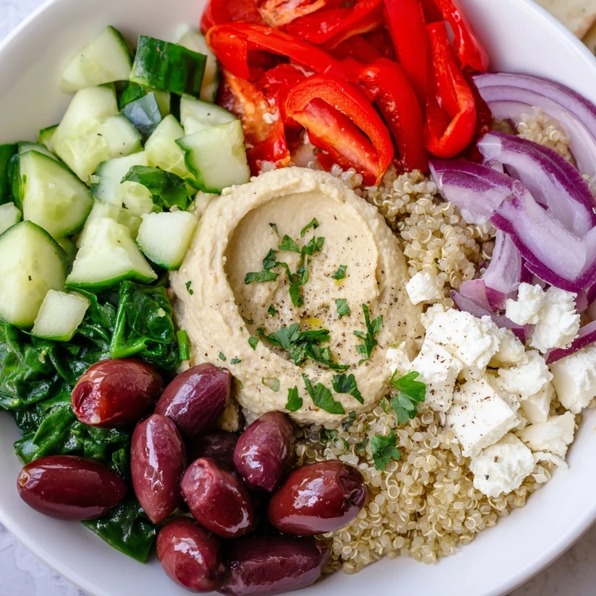 Fluffy quinoa and creamy hummus top vibrant chopped veggies, feta, and Kalamata olives in this Mediterranean Quinoa Bowl. 