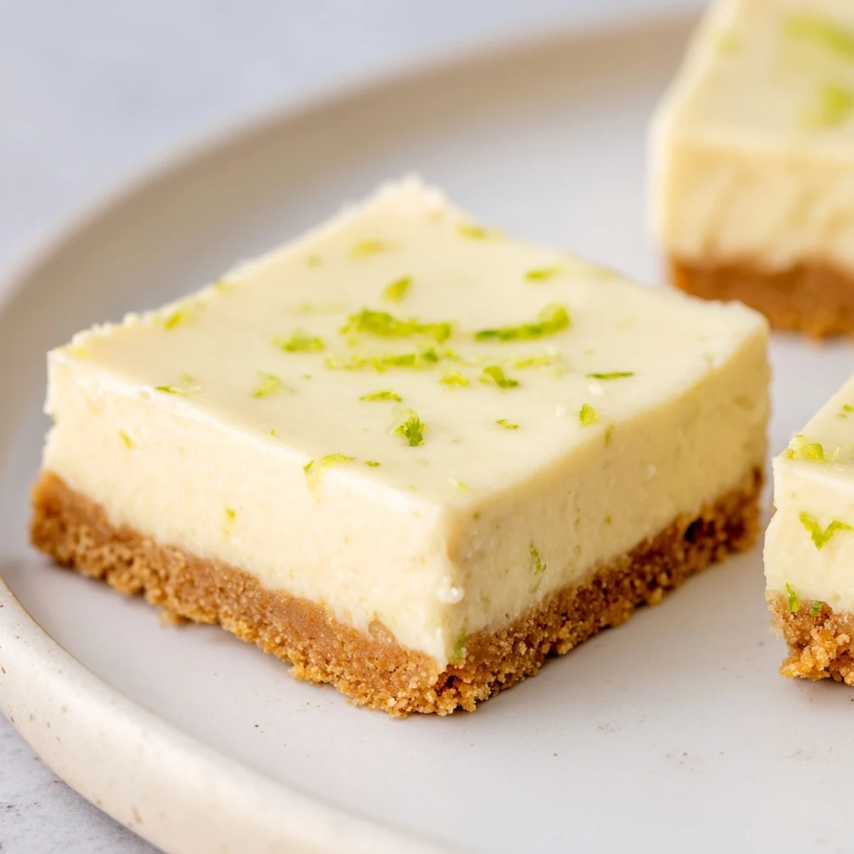 Brightly colored lime bars with a golden graham cracker crust and a dollop of whipped cream, ready to serve chilled.