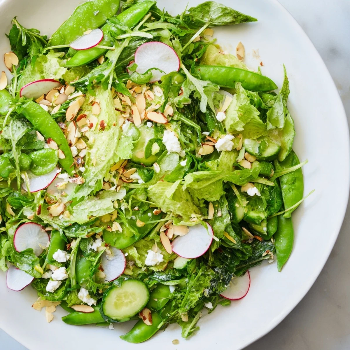 A close-up of Spring Greens Salad with Lemon Vinaigrette, tossed in a glass bowl and finished with crumbled goat cheese.