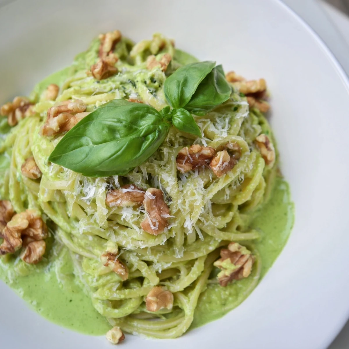 Creamy Avocado and Spinach Pasta with Walnuts served in a white bowl with fresh basil and extra Parmesan.