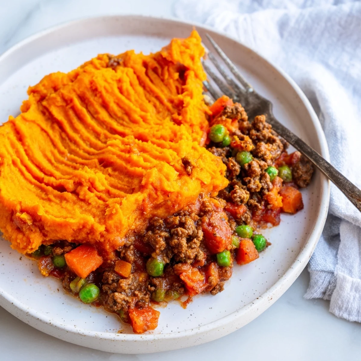 A rustic portion of Beef Shepherds Pie with Sweet Potato Mash on a white plate beside fresh thyme.