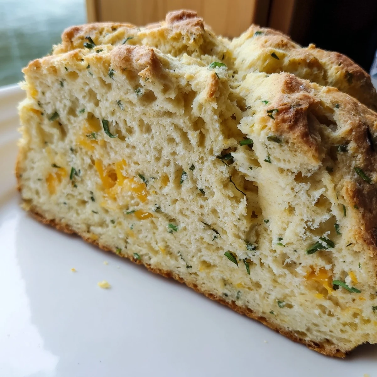 Freshly baked Savory Herbed Cheddar Irish Soda Bread resting on a cooling rack with herbs scattered nearby.
