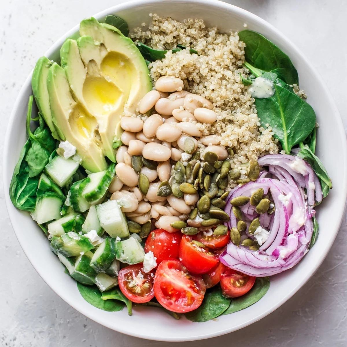 A vibrant Spinach & White Bean Ultimate Protein Power Bowl in a white ceramic bowl, featuring fluffy quinoa, fresh spinach, white beans, cherry tomatoes, and cucumber topped with avocado and pumpkin seeds.