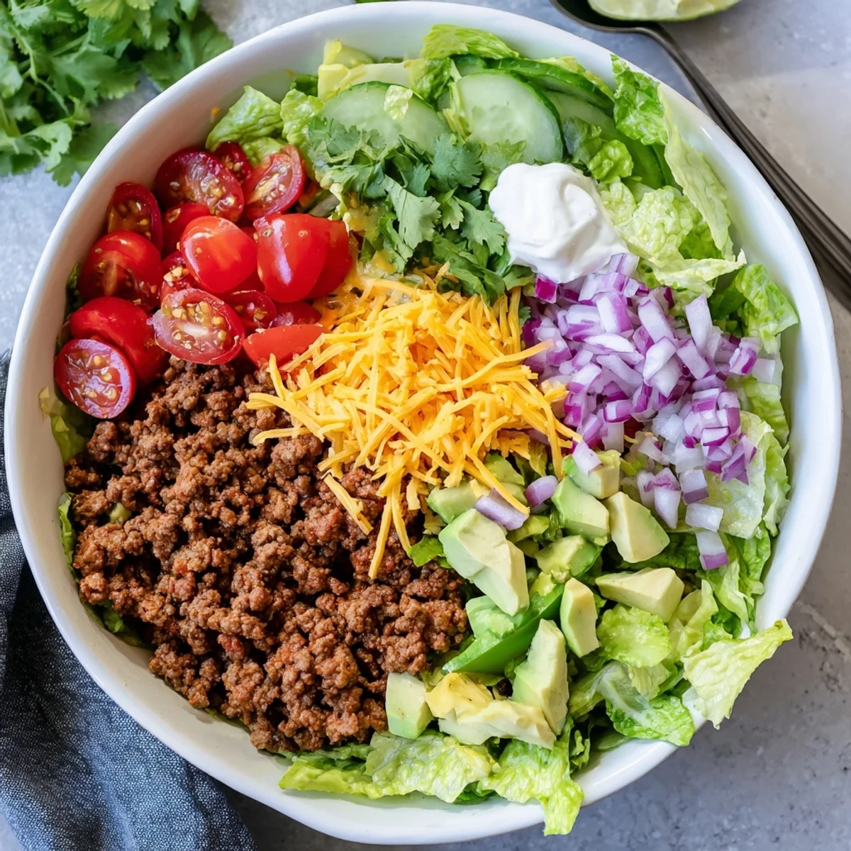 A colorful Low Carb Burrito Bowl with seasoned ground beef, diced avocado, and fresh cherry tomatoes on crisp romaine lettuce.