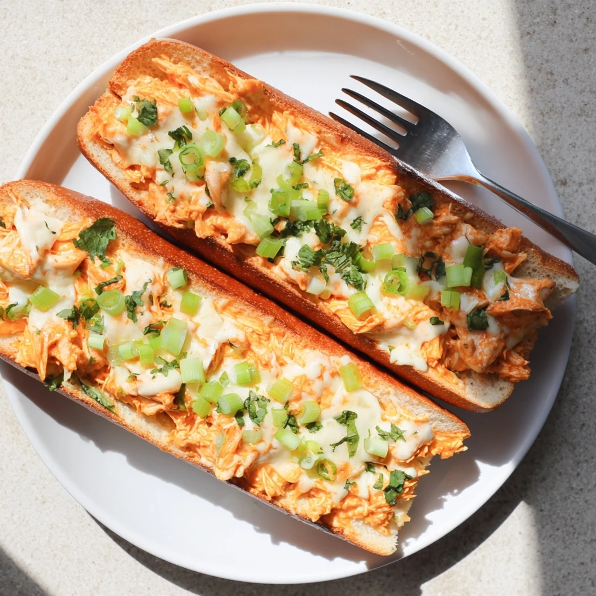 Sliced crosswise, the crispy French bread reveals a hearty filling of spicy buffalo chicken and creamy cheese, perfect for game day gatherings or a comforting family dinner.