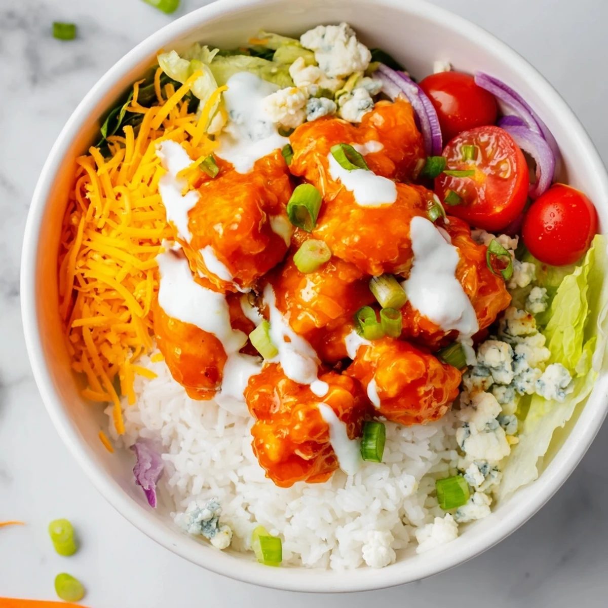 Warm, spicy buffalo chicken sits atop fluffy white rice, drizzled with cool ranch, crisp lettuce, and juicy tomatoes for a vibrant bowl.