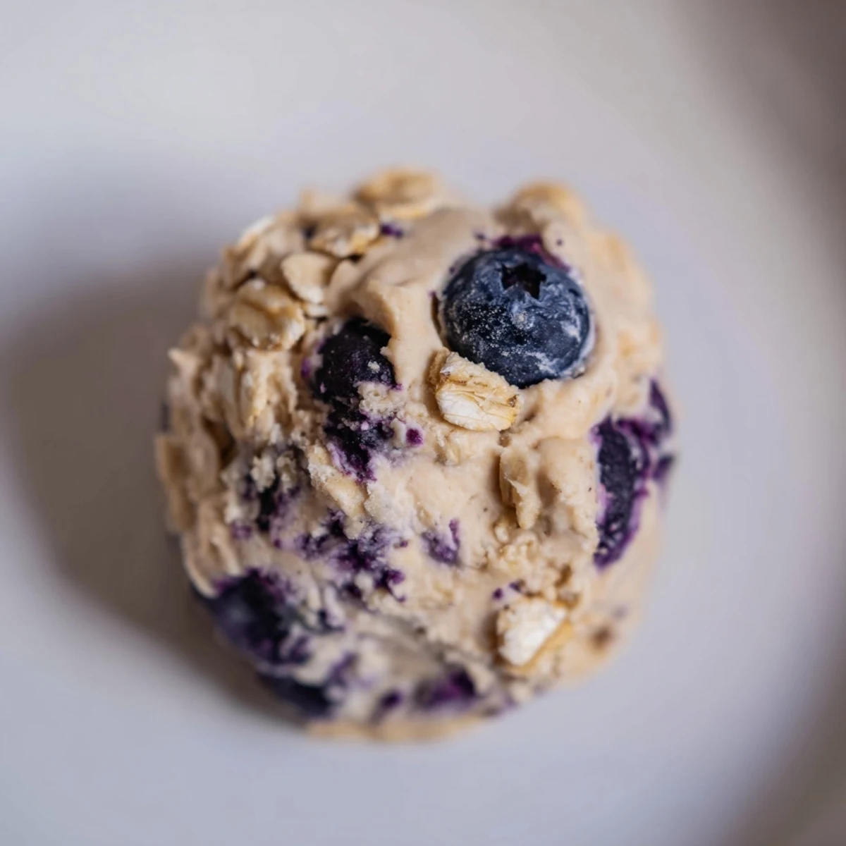 Twelve blueberry cheesecake protein bites are arranged on a parchment-lined tray with fresh blueberries nearby for a healthy snack idea.