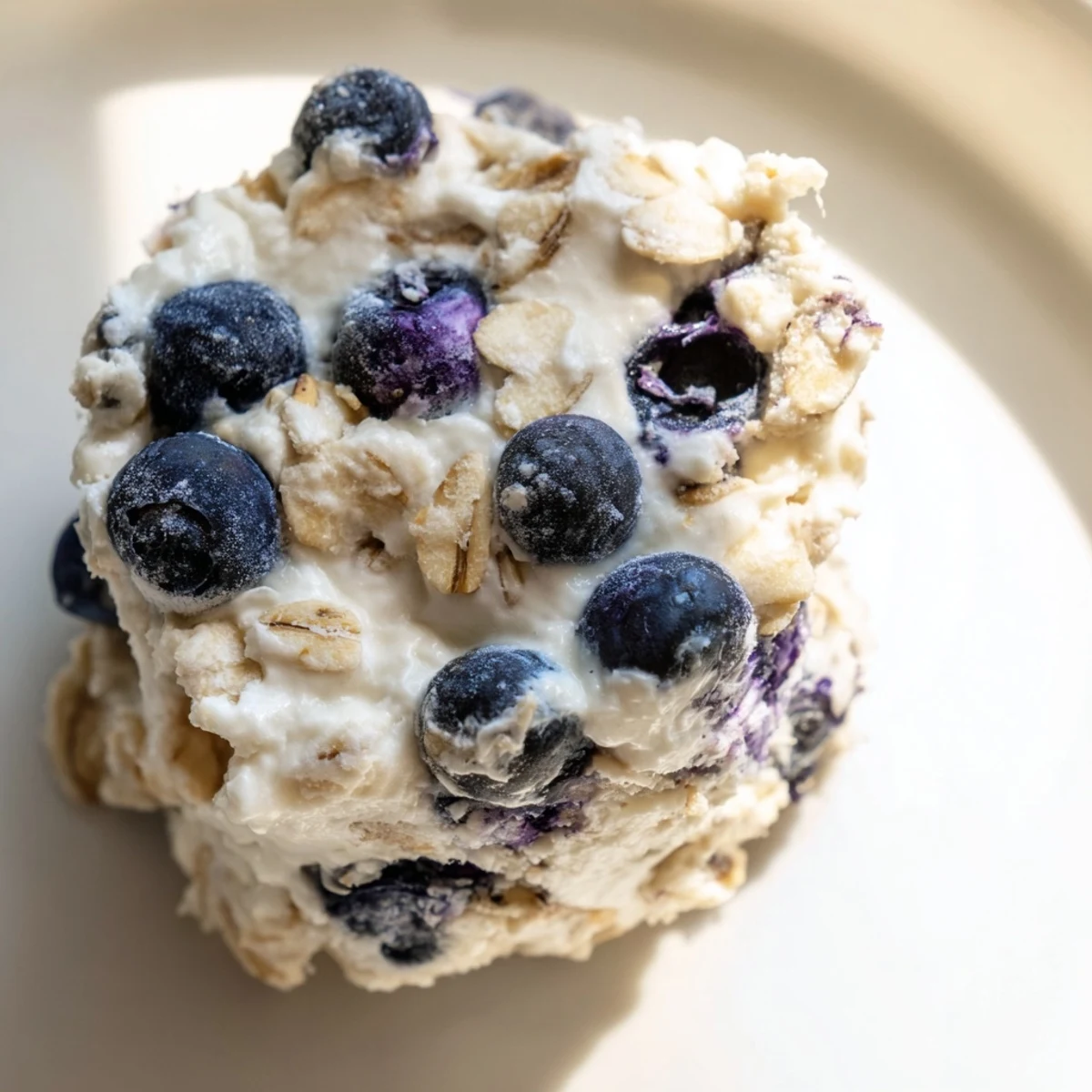 These gluten-free blueberry cheesecake protein bites are displayed in an airtight container with a chilled glass of milk for serving.
