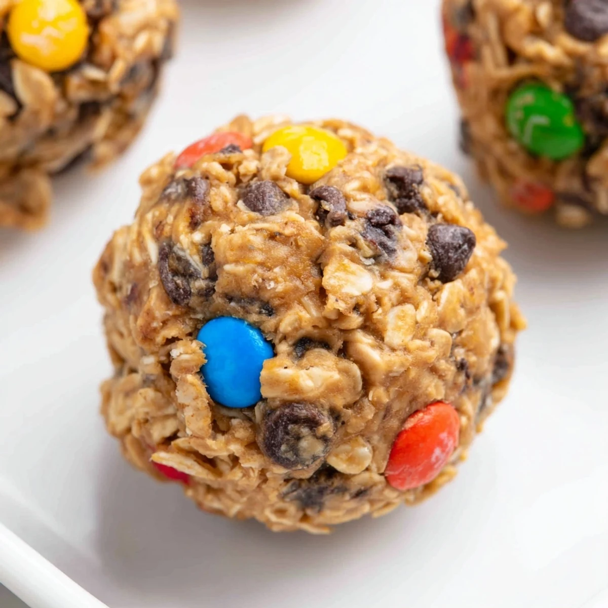 A close-up of colorful Monster Cookie Protein Balls with oats, chocolate chips, and M&Ms on a marble tray.