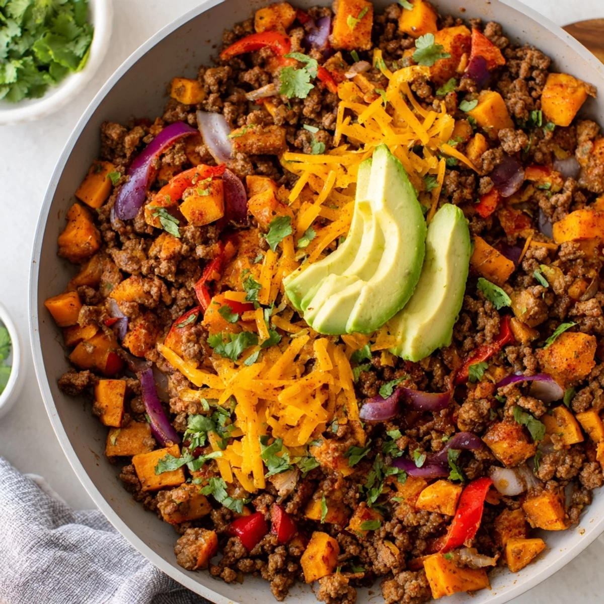 Hearty Southwest ground beef and sweet potato skillet served steaming hot with zesty chili and cumin aromas, garnished with creamy avocado slices