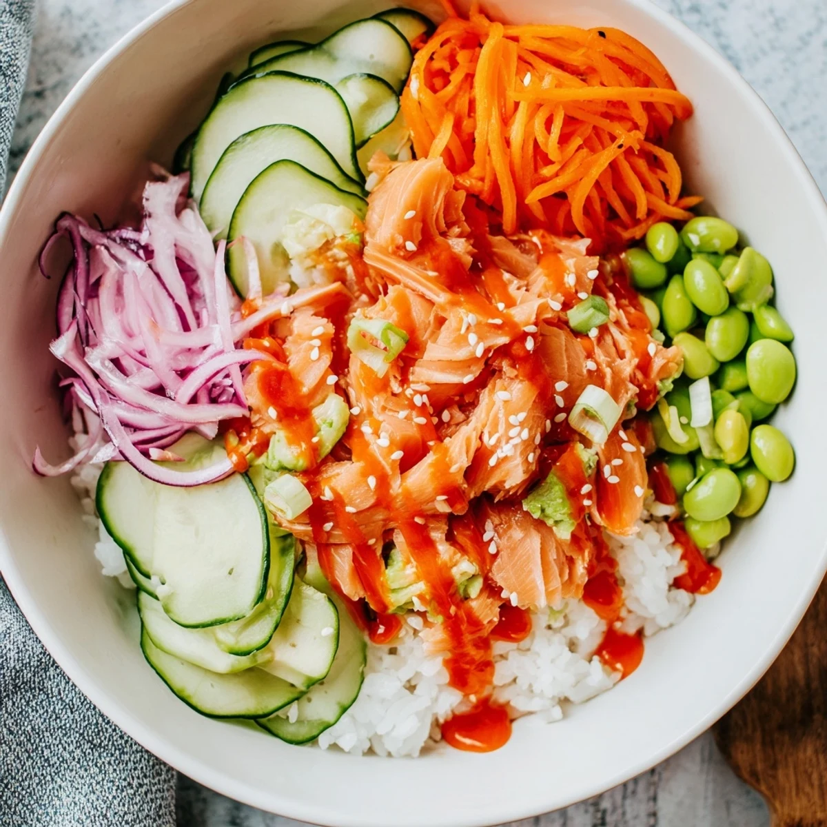 Colorful easy salmon bowl with flaky baked fish, fresh avocado, cucumber, and spicy sriracha mayo drizzle