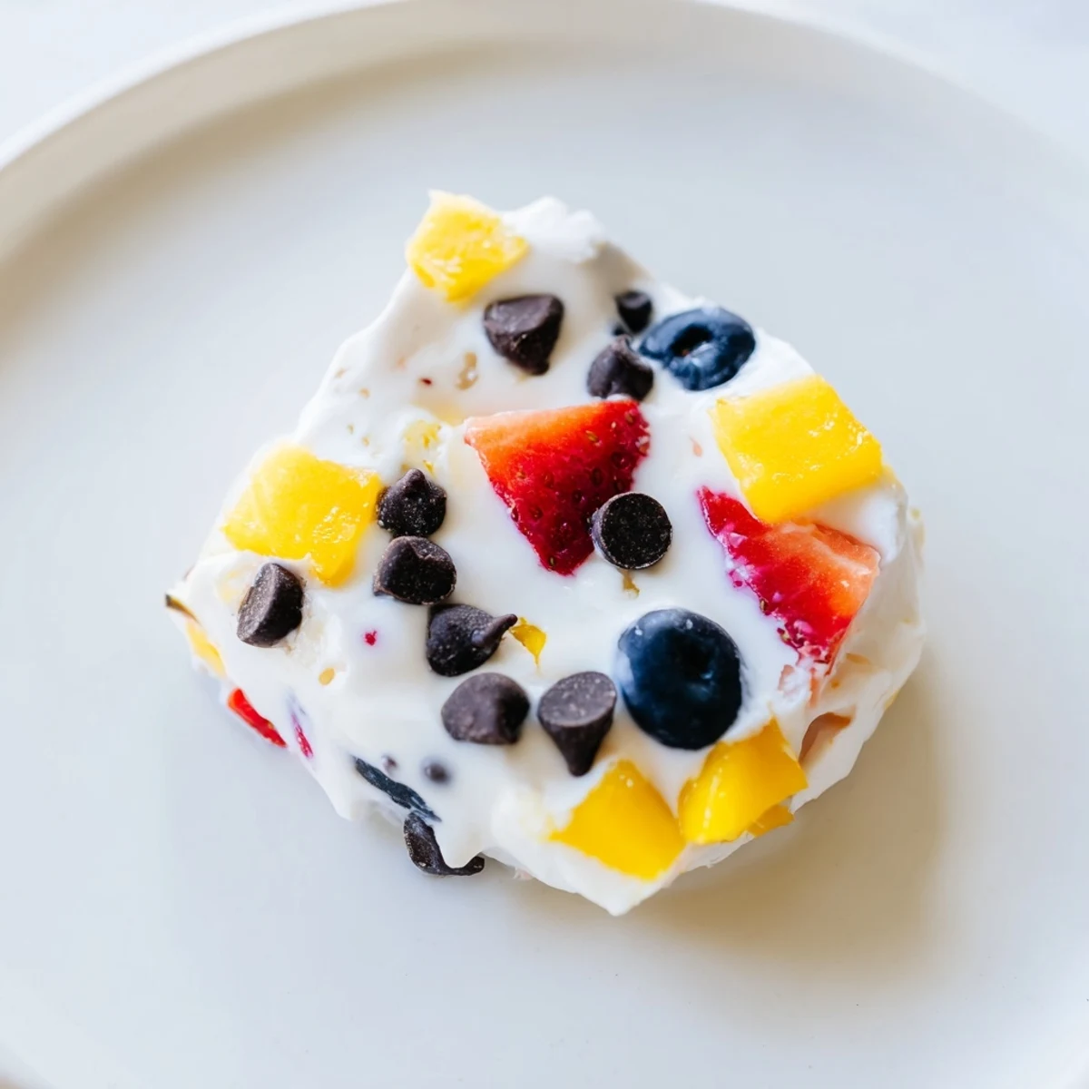Refreshing frozen Greek yogurt bites with vibrant diced fruit in a round bite-sized shape on parchment paper