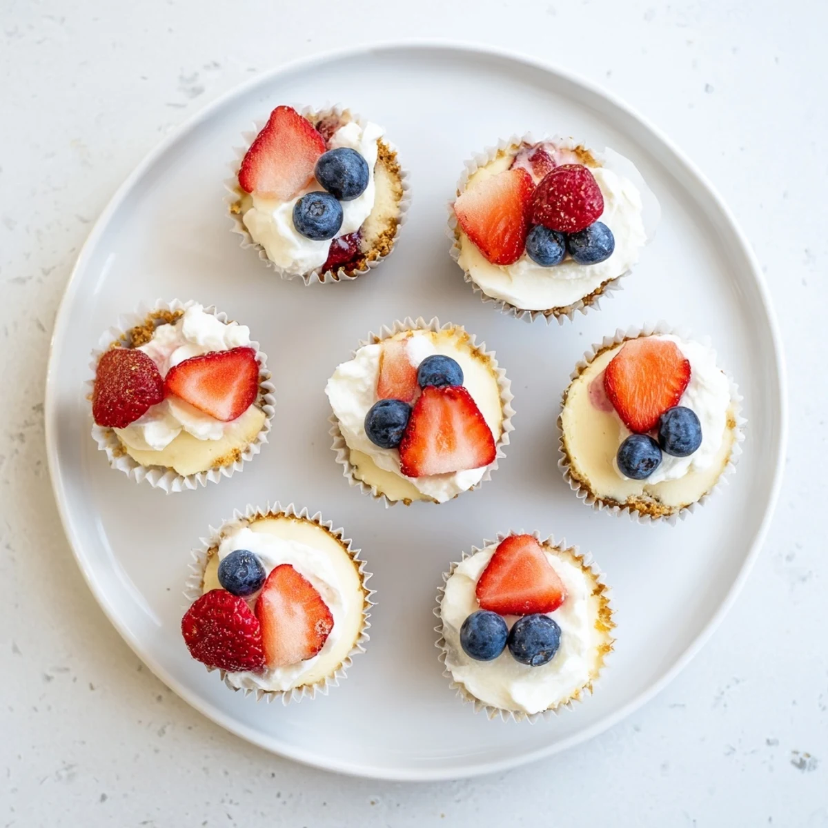 Close up of bite-sized cheesecakes on white serving platter with sour cream topping and colorful fruit