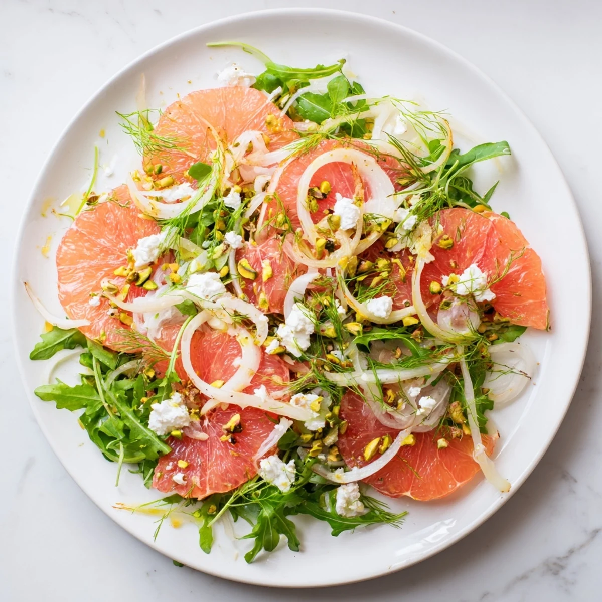 Colorful Grapefruit Goat Cheese Fennel Salad plated with toasted pistachios, grapefruit segments, shaved fennel, and soft goat cheese on baby greens.