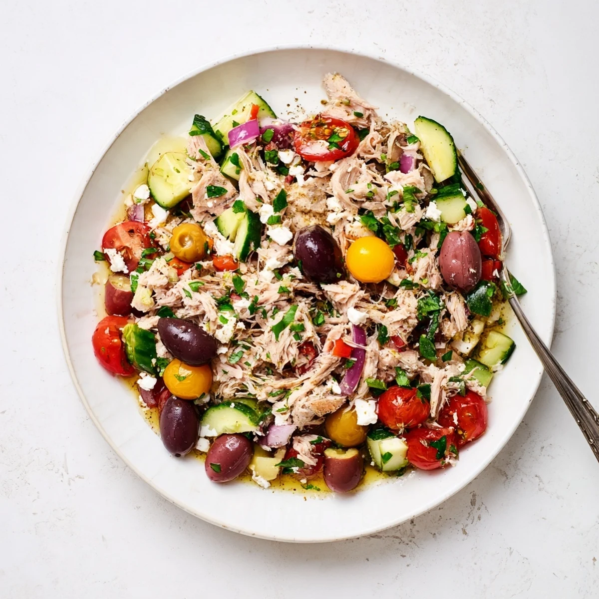 Colorful bowl of Mediterranean tuna salad with fresh tomatoes, cucumber, olives, and herbs.