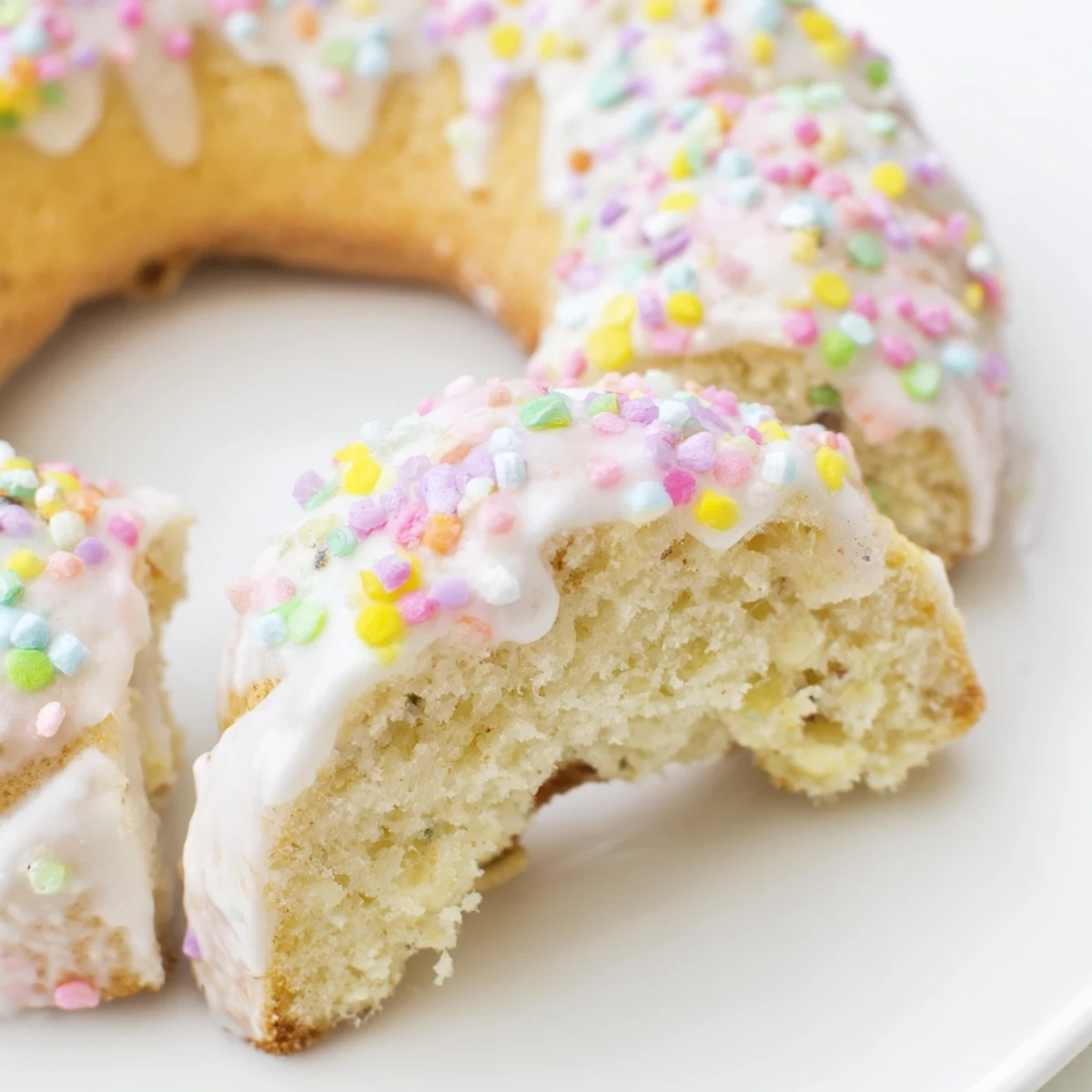 Soft Italian Easter cookies topped with white icing and colorful pastel sprinkles on a wire cooling rack