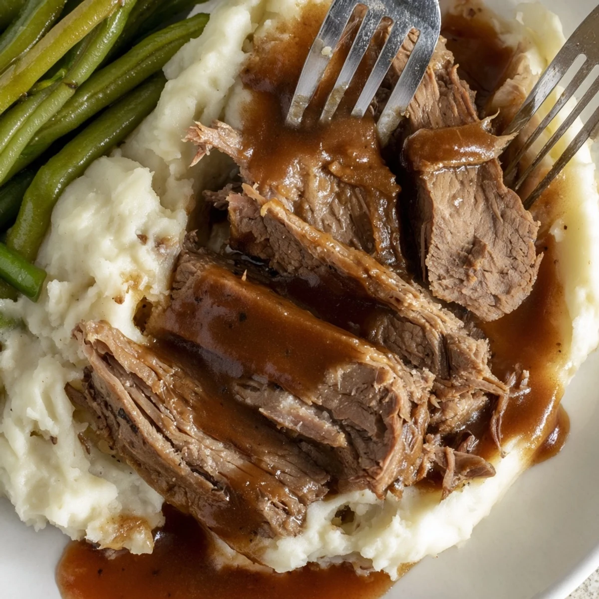 Fork-shredded Southern style pot roast nestled alongside fluffy mashed potatoes and crisp seasoned green beans drizzled with savory homemade beef gravy