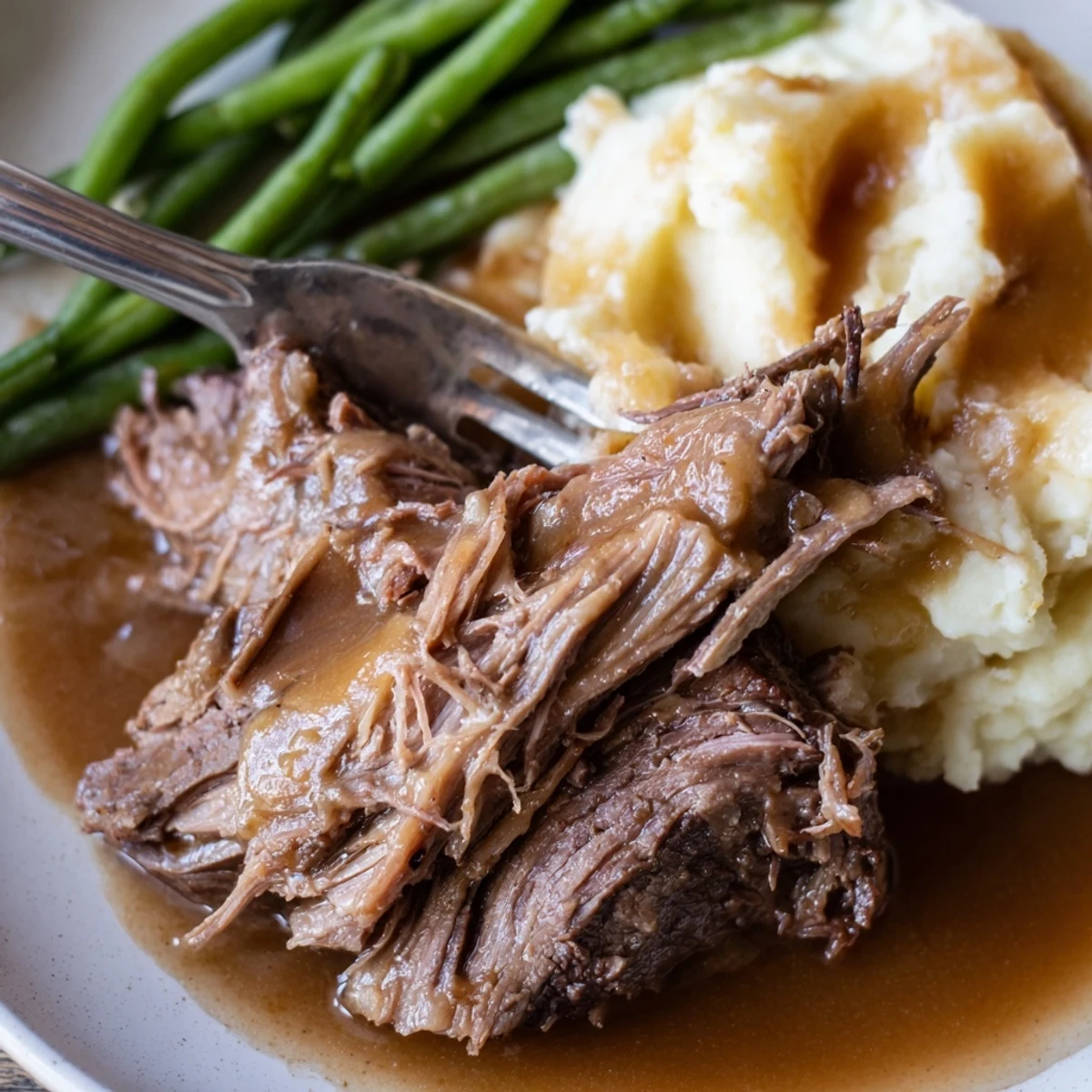 Tender Southern style pot roast with rich gravy served beside creamy mashed potatoes and buttered green beans on a white dinner plate