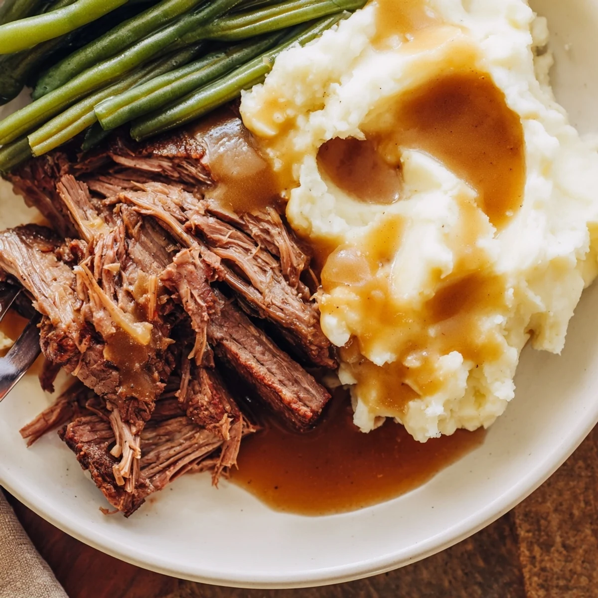 Classic Southern style pot roast plated with golden mashed potatoes and fresh green beans topped with a dark glossy beef gravy sauce