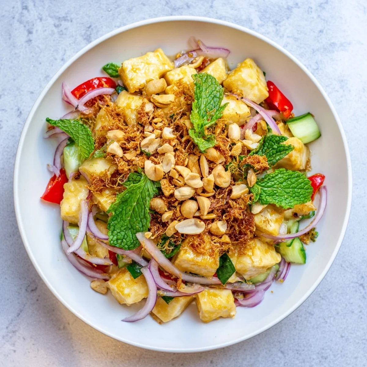 Colorful Burmese tofu salad with fresh herbs, crunchy peanuts, and tangy lime dressing in bowl