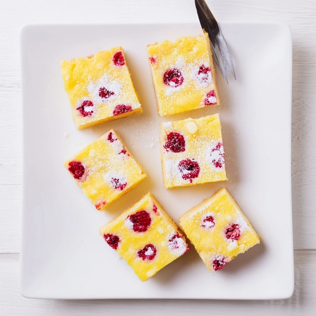 Square lemon raspberry dessert bars with vibrant red berries in yellow custard