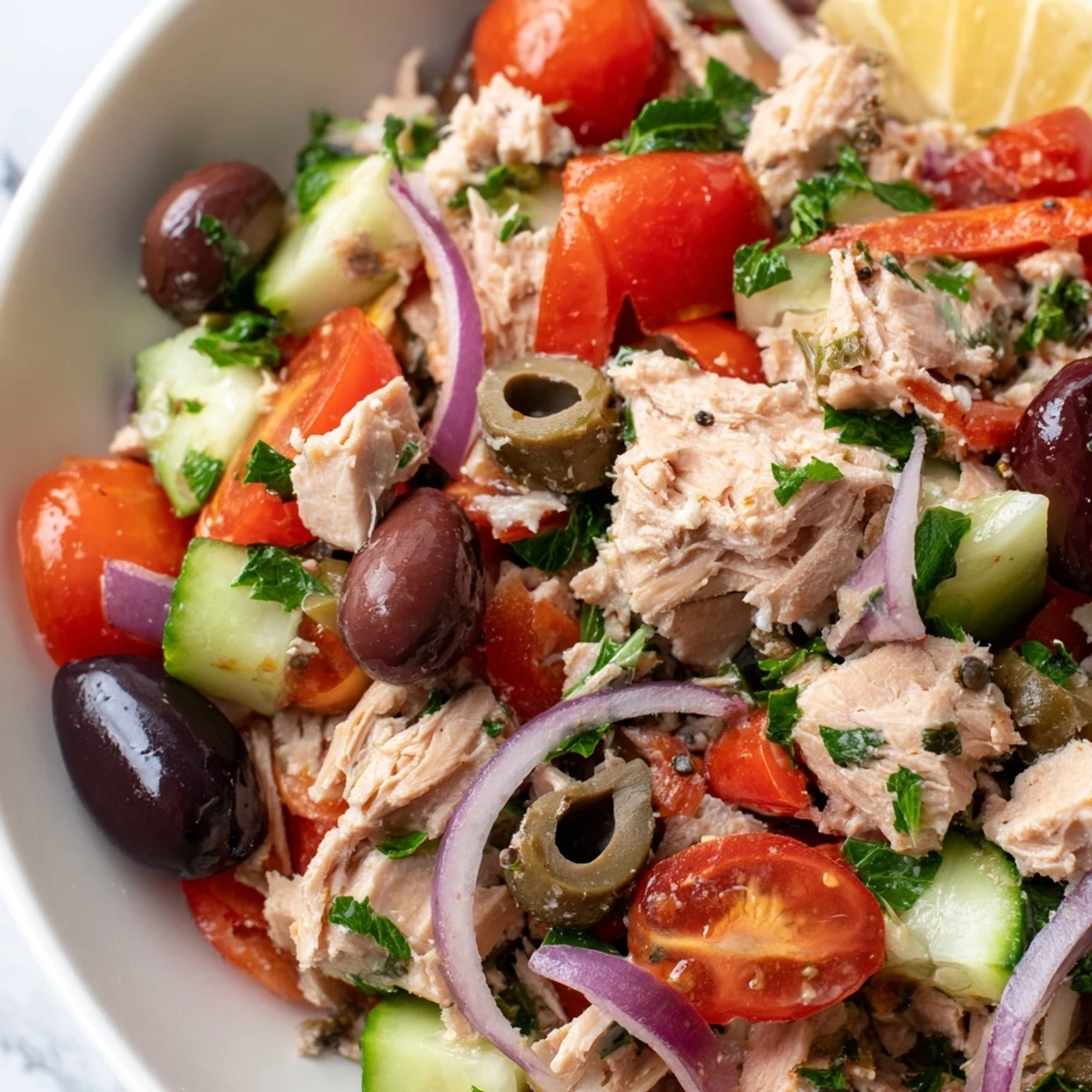 Mediterranean tuna salad in a white bowl with cherry tomatoes, olives, and fresh herbs