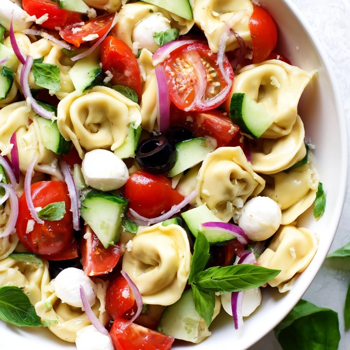 Creamy cheese tortellini salad tossed with crisp vegetables and zesty vinaigrette in white bowl