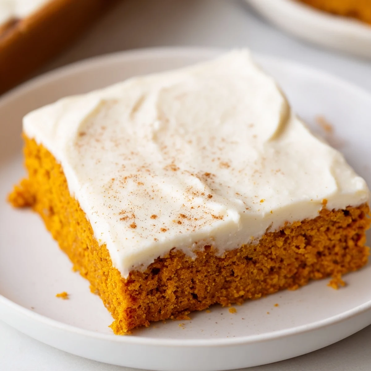 Cream cheese frosted pumpkin bars cut into neat squares on a rustic baking sheet