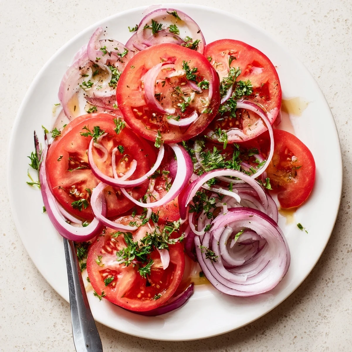 Fresh tomato and onion salad drizzled with olive oil vinaigrette and topped with parsley on a white serving plate