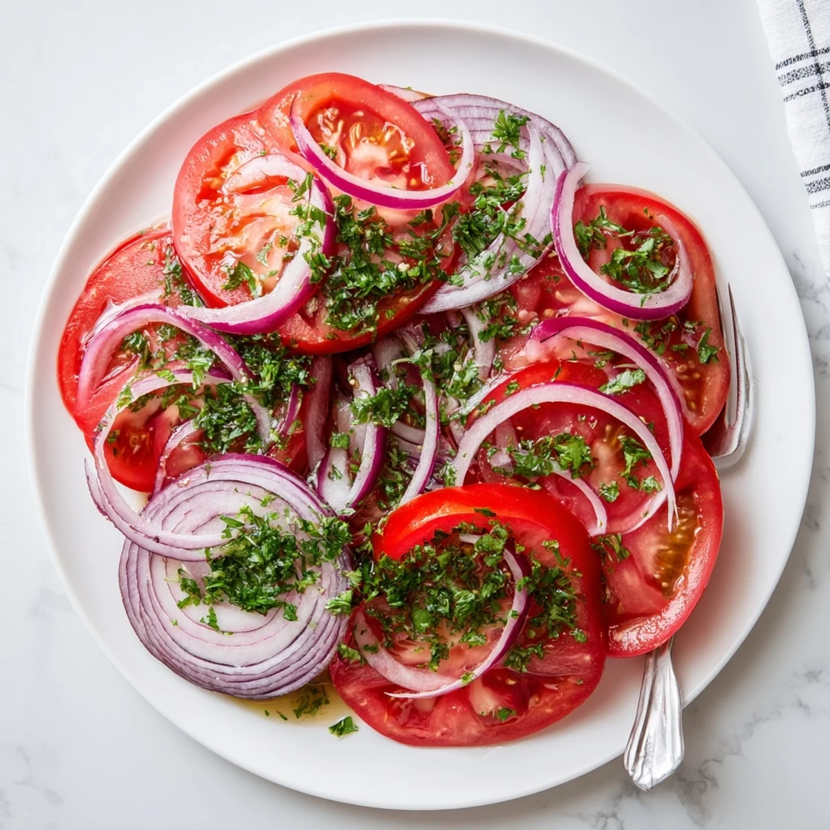 Sliced ripe tomatoes and red onions arranged in a vibrant salad with light dressing and fresh green parsley garnish