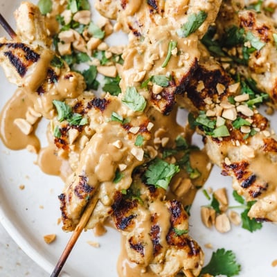 A close-up of Chicken Satay Skewers with Peanut Sauce reveals juicy, char-grilled chicken pieces dripping with rich sauce.