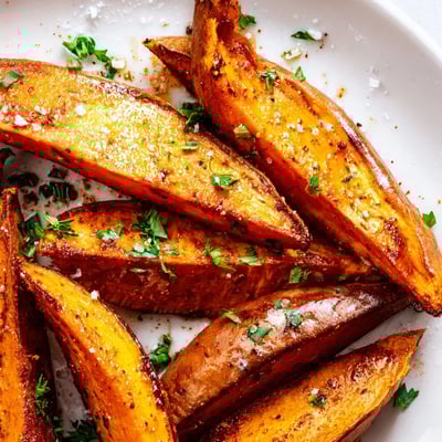 Roasted Sweet Potato Wedges with Paprika, freshly baked and garnished with parsley on a rustic wooden board.
