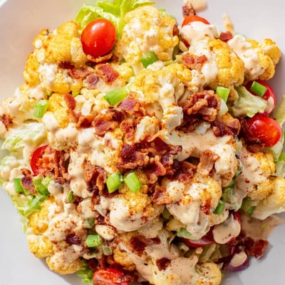 Freshly prepared BLT Cauliflower Salad with chopped romaine, cherry tomatoes, smoky paprika bacon bits, and creamy dressing ready for a light lunch.  