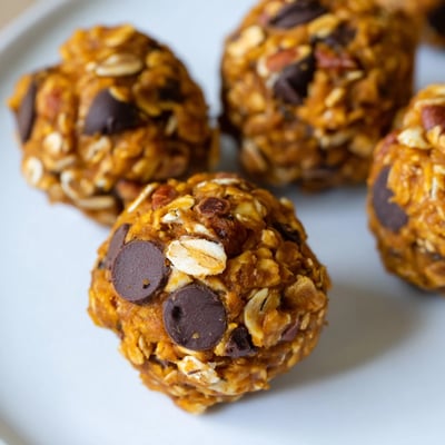Five No Bake High Protein Pumpkin Bites rest on a chilled metal tray beside a mug of steaming spiced tea.