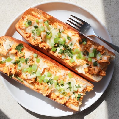Sliced crosswise, the crispy French bread reveals a hearty filling of spicy buffalo chicken and creamy cheese, perfect for game day gatherings or a comforting family dinner.