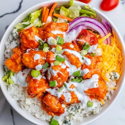 Buffalo Chicken Bowls with creamy ranch dressing, shredded cheddar, carrots, and green onions on a bed of hearty rice, ready to serve.