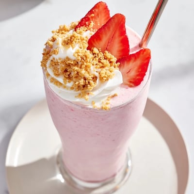Pink strawberry cheesecake milkshake in a tall glass with fresh strawberry slices