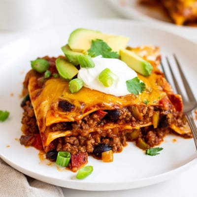 Beef Skillet Enchiladas topped with avocado, green onions, and creamy sour cream
